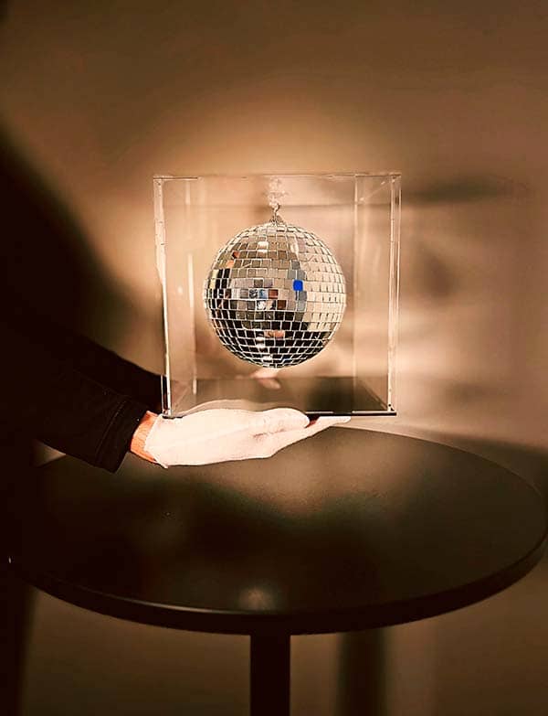 The Moon sculpture – held by hand before installation A gloved hand holding The Moon sculpture by Rosana Auqué inside a transparent acrylic box.
