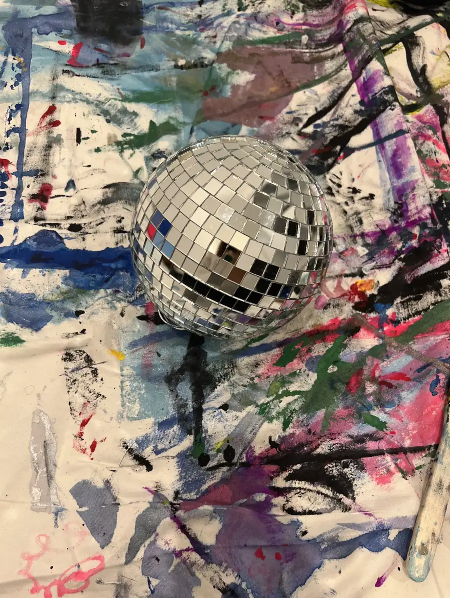 he Moon sculpture in Rosana Auqué’s studio – creation process The reflective sphere of The Moon sculpture by Rosana Auqué resting on a colorful, paint-stained studio canvas during its creation process.